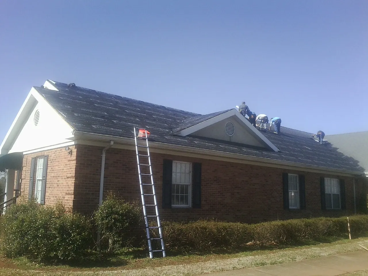 Crew tearing shingles off a brick ranch roof with a ladder set — Emergency Roof Repair work by our crew in Bath
